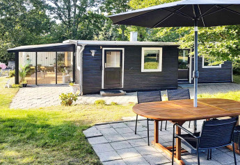 Area esterna della casa vacanze per 4 persone ad Allingåbro, Danimarca, con patio, tavolo e facciata nera.
