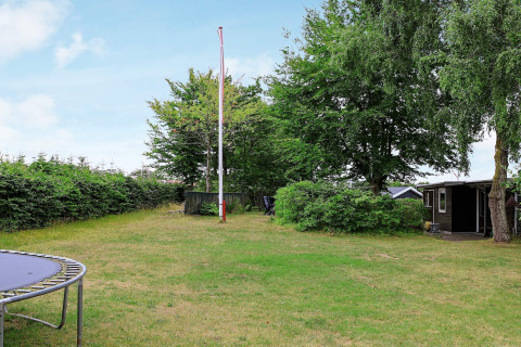 Jardín verde con asta de bandera, trampolín y casa de vacaciones al fondo en Allingåbro, Dinamarca.