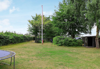 Giardino verde con asta della bandiera, trampolino e casa vacanze sullo sfondo ad Allingåbro, Danimarca.
