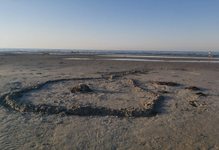 Beach scene at Allingåbro, Denmark featuring a sand drawing in the foreground and calm sea beyond.
