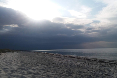 Serena playa en Allingåbro, Dinamarca, con arena clara, cielo nublado y mar tranquilo al atardecer.