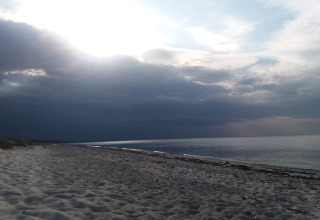 Plage paisible à Allingåbro, Danemark, avec sable clair, mer calme et ciel nuageux en arrière-plan.