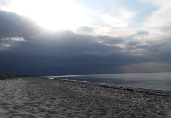 Ruhige Strandlandschaft in Allingåbro, Dänemark, mit Wolkenhimmel und sanften Wellen am Meer.