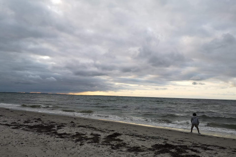 Ein Mensch spaziert am Strand unter bewölktem Himmel nahe der Unterkunft '4 person holiday home in Allingåbro', Dänemark.