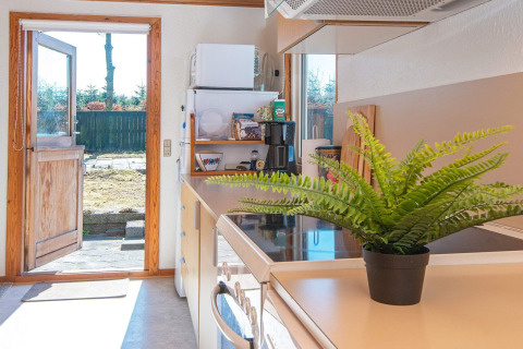 Cucina luminosa in casa vacanze ad Allingåbro, Danimarca, porta aperta sul giardino, pianta verde sul tavolo.