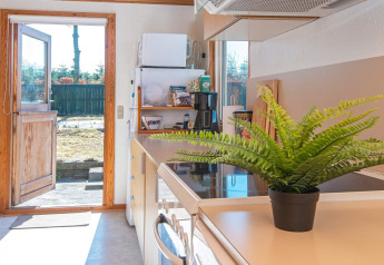 Helles Ferienhaus-Küche in Allingåbro, Dänemark, mit offener Tür zum Garten und grüner Pflanze.