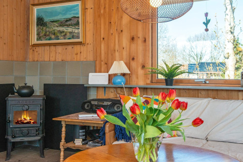 Gemütliches Wohnzimmer im Ferienhaus in Allingåbro, Dänemark mit Kamin, Sofa und Tulpenstrauß.