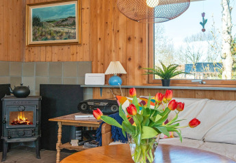 Gemütliches Wohnzimmer im Ferienhaus in Allingåbro, Dänemark mit Kamin, Sofa und Tulpenstrauß.