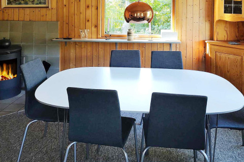 Spisestue med seks stole, hvidt bord, pejs og træpaneler i en feriebolig i Allingåbro, Danmark.
