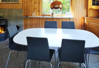 Eetkamer met zes stoelen, witte tafel, open haard en houten wanden in Allingåbro, Denemarken.