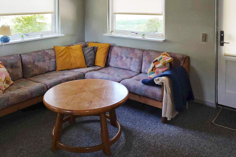 Living room in a holiday home in Allingåbro, Denmark with corner sofa, colorful pillows and round table