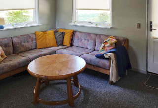 Living room in a holiday home in Allingåbro, Denmark with corner sofa, colorful pillows and round table