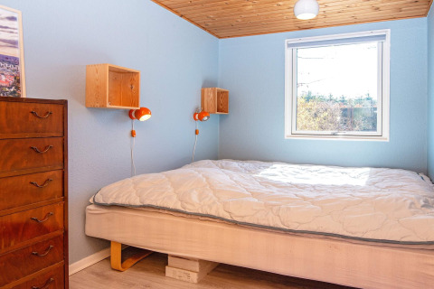 Heldere slaapkamer met blauwe muren, houten plafond, dubbel bed en ladekast in een Allingåbro vakantiehuis.