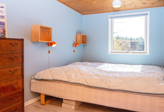 Camera luminosa con pareti blu, soffitto in legno, letto matrimoniale e cassettiera in casa vacanza Allingåbro.