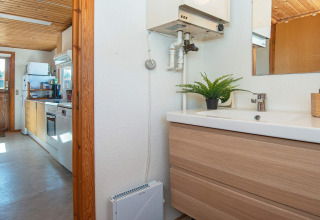 View from bathroom to kitchen in a bright lodge with wood ceiling and modern appliances in Allingåbro, Denmark.
