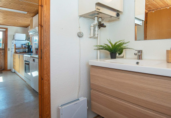 Blick vom Badezimmer in die Küche einer hellen Ferienwohnung mit Holzdecke in Allingåbro, Dänemark.