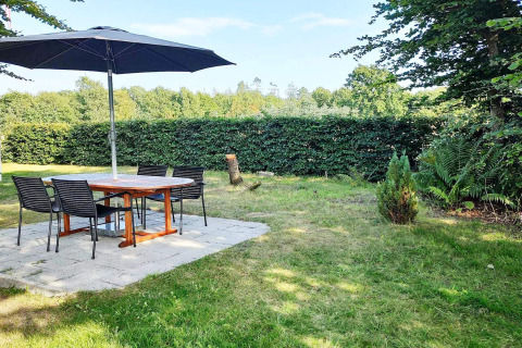 Patio esterno con tavolo rotondo, quattro sedie e ampio ombrellone in un giardino danese verdeggiante.
