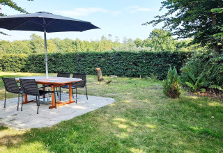 Outdoor patio with round table, four chairs, and a large parasol in a lush Danish garden setting.