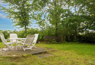 Buitentuin met witte tuinmeubelen, gras, bomen en een bankje bij een vakantiehuis in Allingåbro.