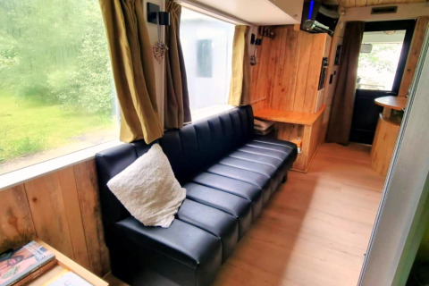 Interieur van de REEBUS-mobiele woning in België met zwarte zetel, houten panelen en groot raam.