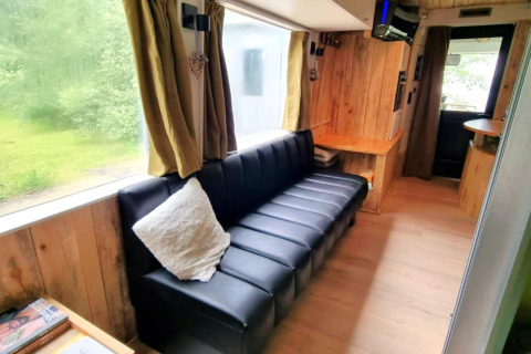 Indvendig billede af REEBUS mobilhome i Belgien med sort sofa, træpaneler og stort vindue.