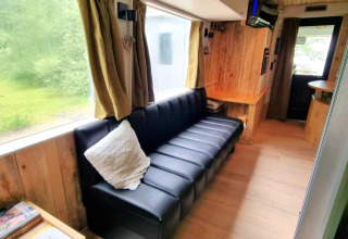 Indvendig billede af REEBUS mobilhome i Belgien med sort sofa, træpaneler og stort vindue.