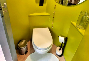 Modern toilet in het REEBUS mobiel huis in België, met felgroene muren en zwarte toiletaccessoires.