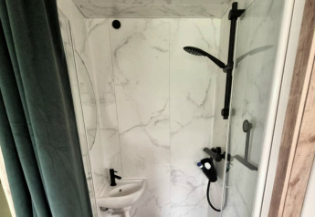 Moderne badkamer in het REEBUS-mobilhome in België met douche, kleine wastafel en marmeren wanden.