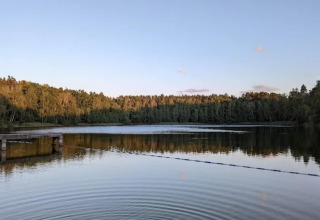 Uitzicht op een stille vijver met een steiger en omringende bomen, gefotografeerd bij een glamping bij zonsondergang.