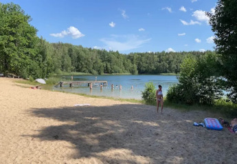 Zandstrand en meer aan een glampingverblijf, mensen zwemmen en liggen in de zon tussen bomen.
