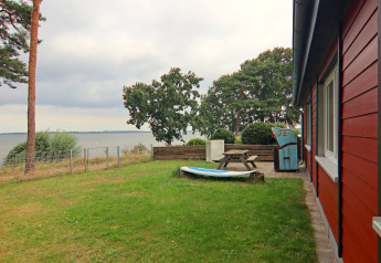 Grasveld en terras bij de rode lodge 'Am Strand' met uitzicht op meer en bomen in Duitsland.
