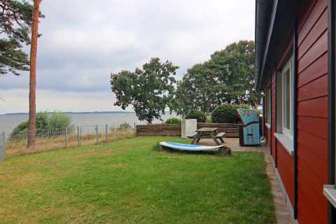 Grasveld en terras bij de rode lodge 'Am Strand' met uitzicht op meer en bomen in Duitsland.