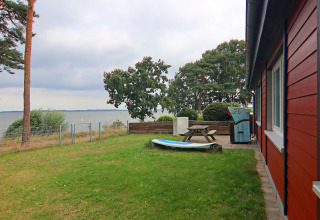 Grasveld en terras bij de rode lodge 'Am Strand' met uitzicht op meer en bomen in Duitsland.
