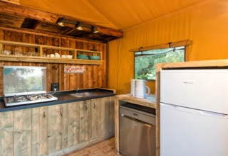 Rustikt køkken i Safari Lodge telte med træmøbler, gaskomfur og køleskab på Weekend Glamping Resort i Italien.