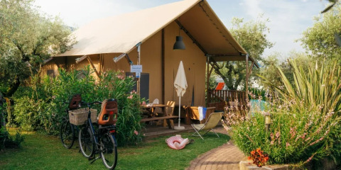 Safari Lodge telt ved Weekend Glamping Resort i Italien, omgivet af grønne planter, cykler og haveudstyr.