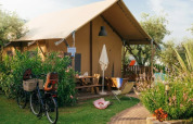 Safari Lodge telt ved Weekend Glamping Resort i Italien, omgivet af grønne planter, cykler og haveudstyr.