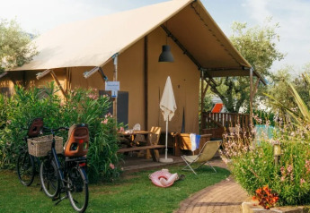 Safari Lodge telt ved Weekend Glamping Resort i Italien, omgivet af grønne planter, cykler og haveudstyr.