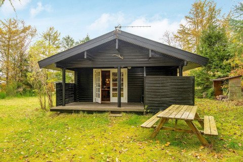 Sort træhytte med overdækket veranda, havebord og grønne omgivelser ved Beautiful cottage near the river.