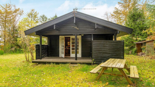 Schwarzes Holzhaus mit Veranda und Picknicktisch im Garten bei Beautiful cottage near the river.