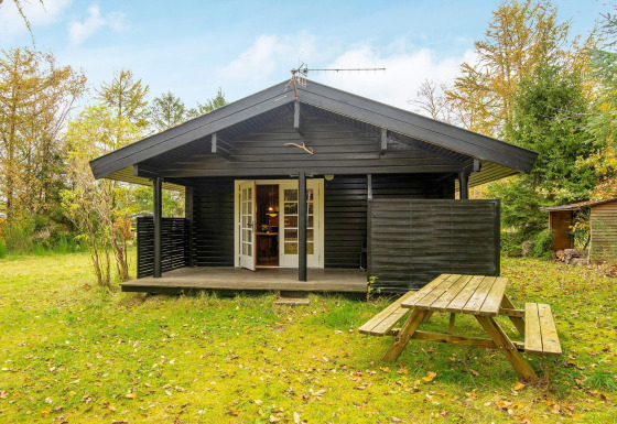 Zwarte houten chalet met overdekt terras en picknicktafel bij Beautiful cottage near the river.