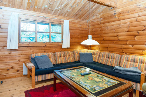 Knusse woonkamer met houten wanden, hoekzetel en sierlijke tafel in een Deense cottage aan de rivier.