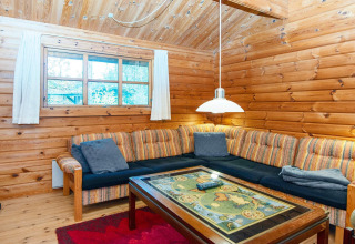 Knusse woonkamer met houten wanden, hoekzetel en sierlijke tafel in een Deense cottage aan de rivier.