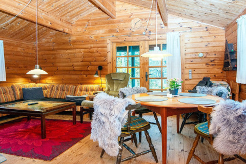 Hyggelig stue i en bjælkehytte i Danmark med træmøbler, sofa, spisebord og varm belysning.