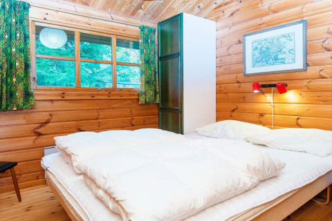 Gezellige houten slaapkamer in een huisje in Denemarken met dubbel bed, groene gordijnen en rode lamp.