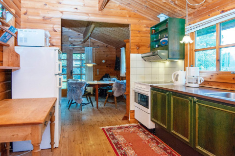 Et hyggeligt køkken i en træhytte med grønne skabe, spisebord og vindue med udsigt til naturen.