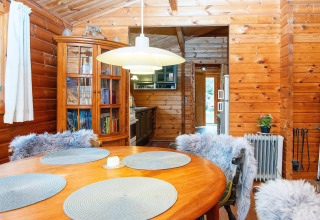 Knusse eetruimte in een houten cottage met ronde tafel, stoelen met bont en zicht op de keuken.