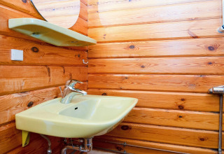 Badkamer met gele lavabo, plank en spiegel, met houten wandpanelen in een Deens vakantiehuis.