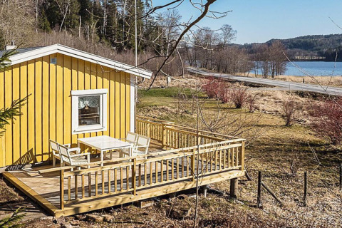 Gele chalet met houten terras aan een meer en weg in Hällevadsholm, Zweden, omringd door natuur.