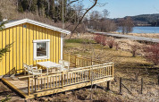 Gul hytte med terrasse og havemøbler nær en sø og landevej i Hällevadsholm, Sverige, omgivet af natur.