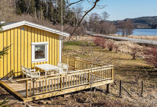 Gele vakantiehuisje met houten terras aan een meer en weg in Hällevadsholm, Zweden, landelijke omgeving.